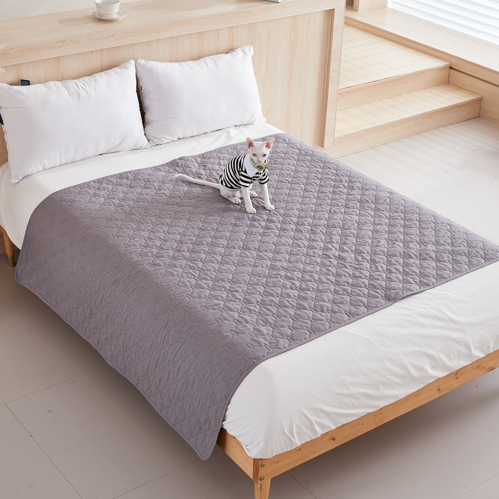 Dark gray quilted pet blanket laid across the foot of a bed